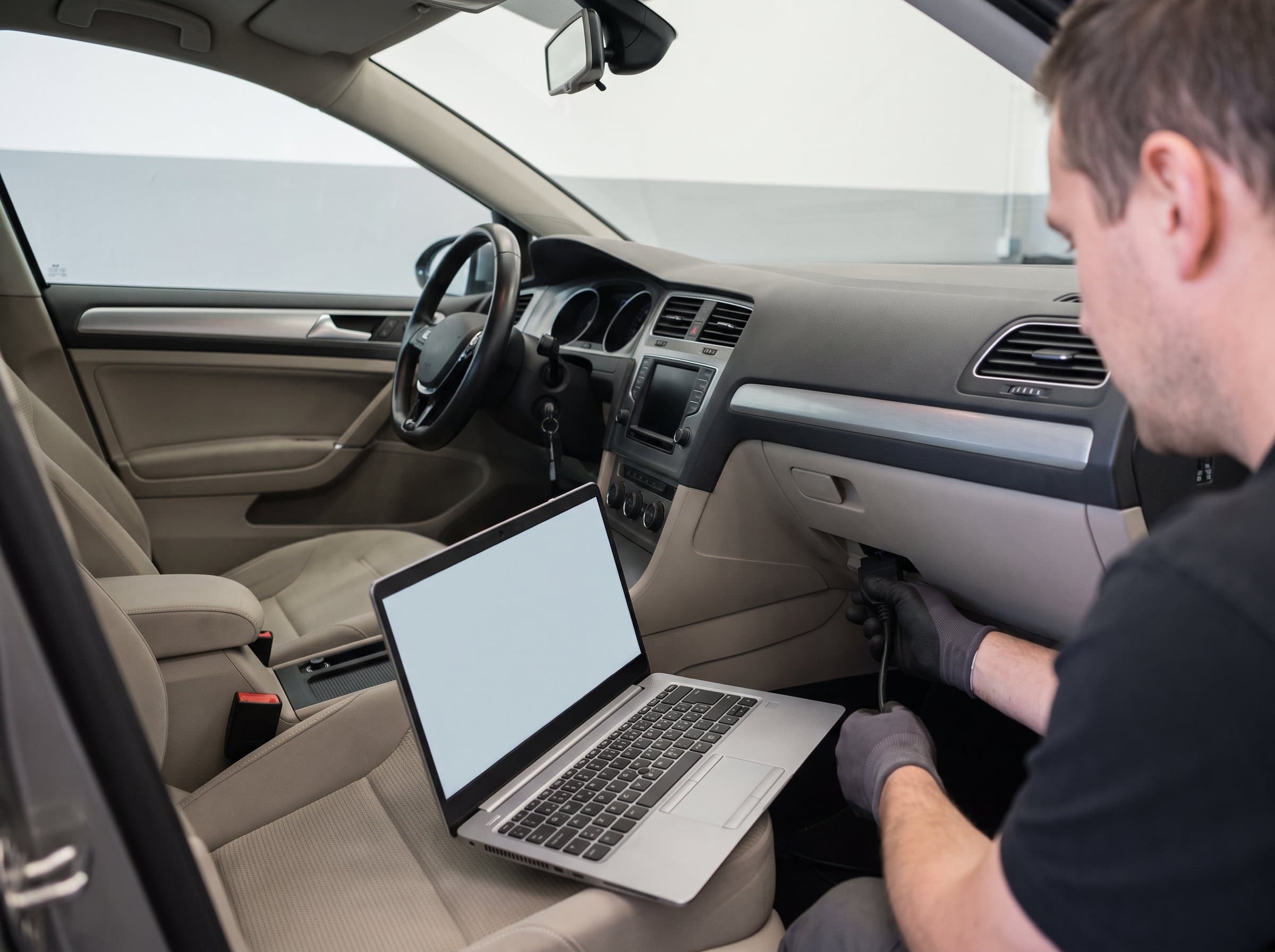 Ein Diagnosekabel wird unter dem Armaturenbrett eingesteckt, der Laptop liegt auf dem Sitz